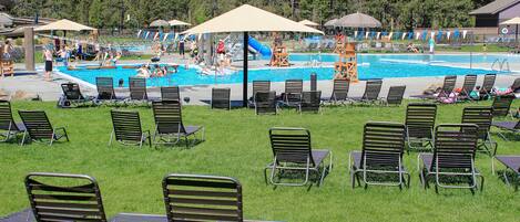 A pool area with multiple lounge chairs and umbrellas, surrounded by a grassy area and trees.