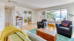 A living room with a sofa, armchair, coffee table, and a view of the outdoors. - Modern, river-view home with 2 decks, Ping-Pong, fireplace & washer/dryer (Stevenson)