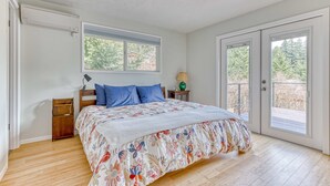 A bedroom with a bed, a nightstand, a lamp, a window, and a door leading to an outdoor area. - Modern, river-view home with 2 decks, Ping-Pong, fireplace & washer/dryer (Stevenson)