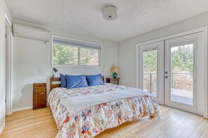 A bedroom with a bed, a nightstand, a lamp, a window, and a door leading to an outdoor area. - Modern, river-view home with 2 decks, Ping-Pong, fireplace & washer/dryer (Stevenson)