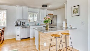 A modern kitchen with white cabinets, a central island with stools, a refrigerator, and a window. - Modern, river-view home with 2 decks, Ping-Pong, fireplace & washer/dryer (Stevenson)