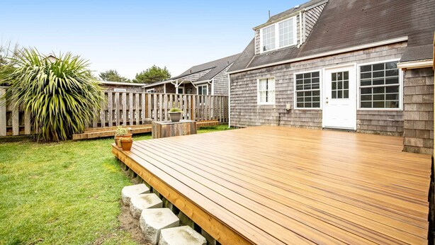 A wooden deck with a grassy yard and a house with a white door and windows. - Charming dog-friendly cottage with sauna, easy beach access, deck & yard (Gearhart)