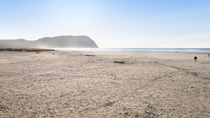 A wide sandy beach with a clear sky and distant mountains. - Charming dog-friendly cottage with sauna, easy beach access, deck & yard (Gearhart)
