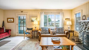 A cozy living room with a red sofa, a wooden coffee table, and a stone fireplace. - Charming dog-friendly cottage with sauna, easy beach access, deck & yard (Gearhart)