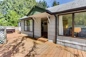 A wooden deck with a covered porch, a wooden bench, and a view of a forested area.