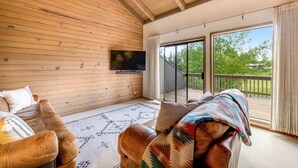 En inredning med träpanel, en takfläkt, en tv som är monterad på väggen, en soffa med en filt och en utsikt genom en glasdörr ut till en uteplats.