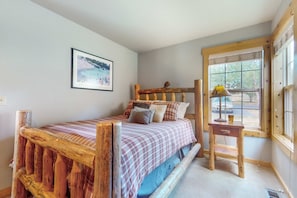 A bedroom with a bed, a bedside table, a window, and a framed picture on the wall.