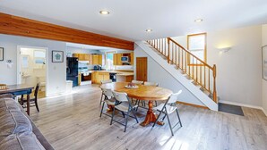 A spacious living area with a dining table, a staircase, and a kitchen in the background. - Dog-friendly cottage with pool table, fast WiFi, fireplace, W/D - walk to beach (Long Beach)