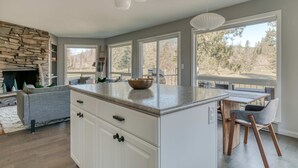 A modern kitchen with a large island, white cabinetry, and a stone fireplace. - Mountain-view condo on the golf course with WiFi, private W/D & gas grill (Welches)