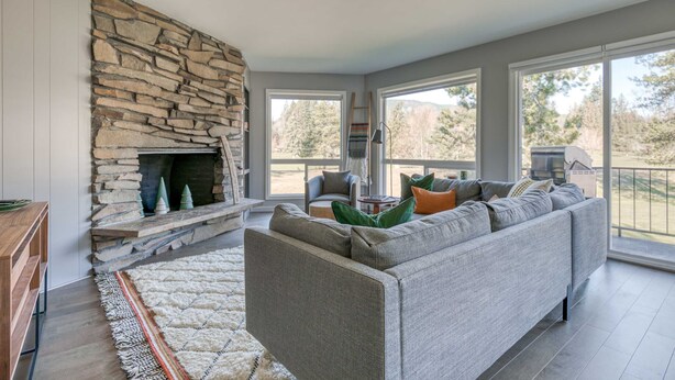 A living room with a stone fireplace, a gray sofa, and large windows. - Mountain-view condo on the golf course with WiFi, private W/D & gas grill (Welches)