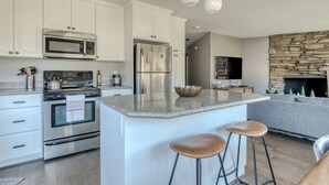 A modern kitchen with white cabinetry, stainless steel appliances, a granite countertop, and a stone fireplace. - Mountain-view condo on the golf course with WiFi, private W/D & gas grill (Welches)