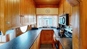 Une cuisine avec des meubles de rangement en bois, un plan de travail noir, une cuisinière et un four à micro-ondes.