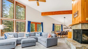 A modern living room with a sectional sofa, large windows, a stone fireplace, and a dining area. - House in Black Butte Ranch with shared amenities (Black Butte Ranch)