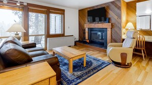 A living room with a fireplace, leather sofa, wooden coffee table, and a chair. - Mountain view condo with a fireplace, WiFi, partial AC, shared hot tub & pool (Bend)