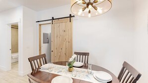 A dining area with a wooden table, chairs, a chandelier, and a sliding barn door. - Stunner apt with fireplace, grill, partial ocean views & partial AC (Gold Beach)