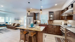 A modern kitchen with dark wood cabinets, a granite countertop, stainless steel appliances, and pendant lighting. - Stunner apt with fireplace, grill, partial ocean views & partial AC (Gold Beach)