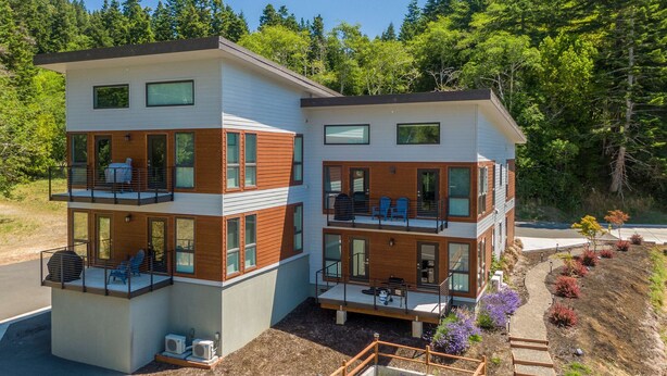 A modern two-story house with balconies, large windows, and a landscaped garden. - Stunner apt with fireplace, grill, partial ocean views & partial AC (Gold Beach)