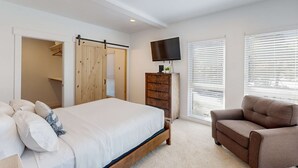 A bedroom with a bed, a dresser, a TV, and a window with blinds. - Stunner apt with fireplace, grill, partial ocean views & partial AC (Gold Beach)