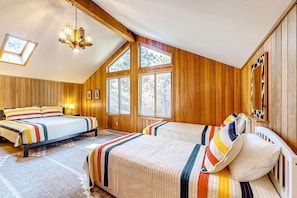 A bedroom with two beds, wooden walls, a sloped ceiling, and large windows.