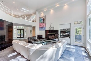 A spacious living area with a high ceiling, a fireplace, a glass coffee table, and a white sofa. - Stylish & secluded home with a washer&dryer, fireplace, & resort amenity access (Black Butte Ranch)