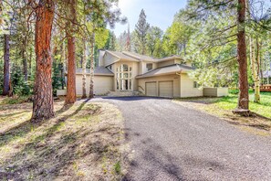 A two-story house with a driveway, surrounded by tall pine trees. - Stylish & secluded home with a washer&dryer, fireplace, & resort amenity access (Black Butte Ranch)