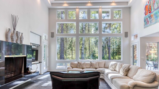 A modern living room with a sectional sofa, a fireplace, and large windows offering a forest view. - Stylish & secluded home with a washer&dryer, fireplace, & resort amenity access (Black Butte Ranch)