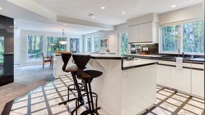 A modern kitchen with a central island, bar stools, and large windows. - Stylish & secluded home with a washer&dryer, fireplace, & resort amenity access (Black Butte Ranch)