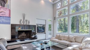 A modern living room with a fireplace, sofa, and large windows. - Stylish & secluded home with a washer&dryer, fireplace, & resort amenity access (Black Butte Ranch)