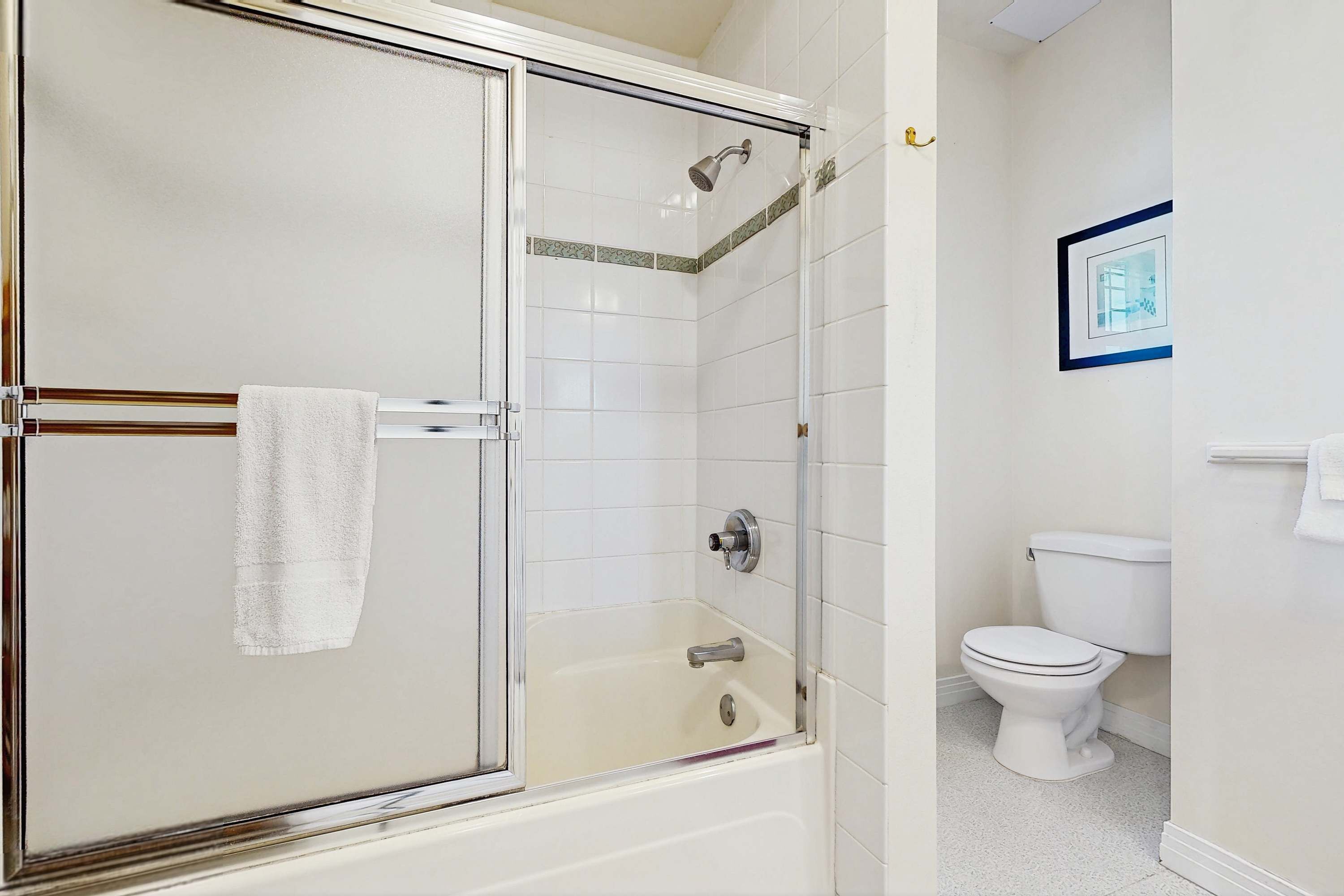 A bathroom with a glass-enclosed shower, a white toilet, and a framed picture on the wall.