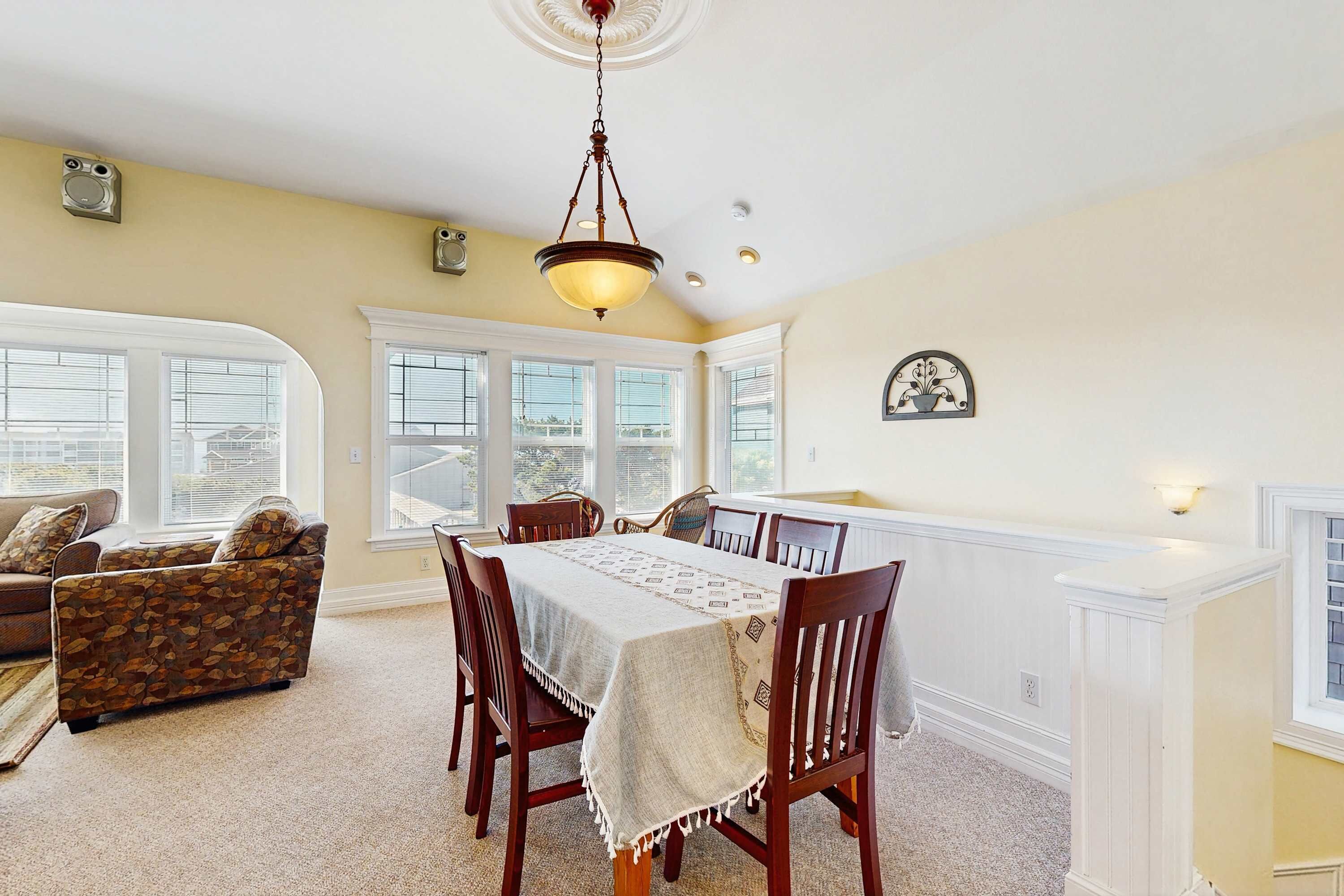 A dining area with a table set for four, surrounded by wooden chairs, a sofa, and a window with blinds.