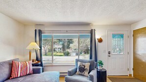 Ein Wohnzimmer mit Sofa, Sessel, Lampe und Blick durch ein großes Fenster.