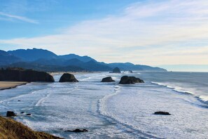 A coastal landscape with rocky formations, a beach, and distant mountains. - Lovely cottage near the beach with free WiFi, cable, and outdoor deck (Cannon Beach)