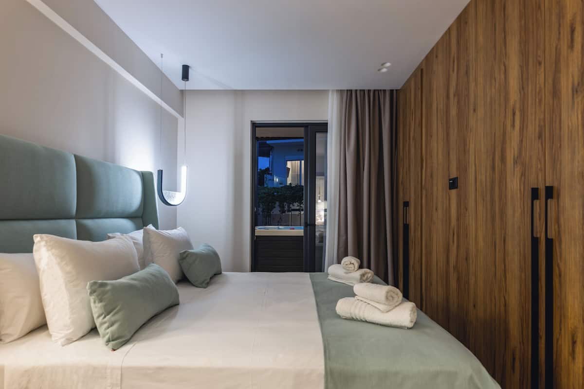 Una habitación de hotel moderna con una cama grande, un panel de madera decorativo y una vista a través de una puerta, con un cielo nocturno visible desde el exterior.