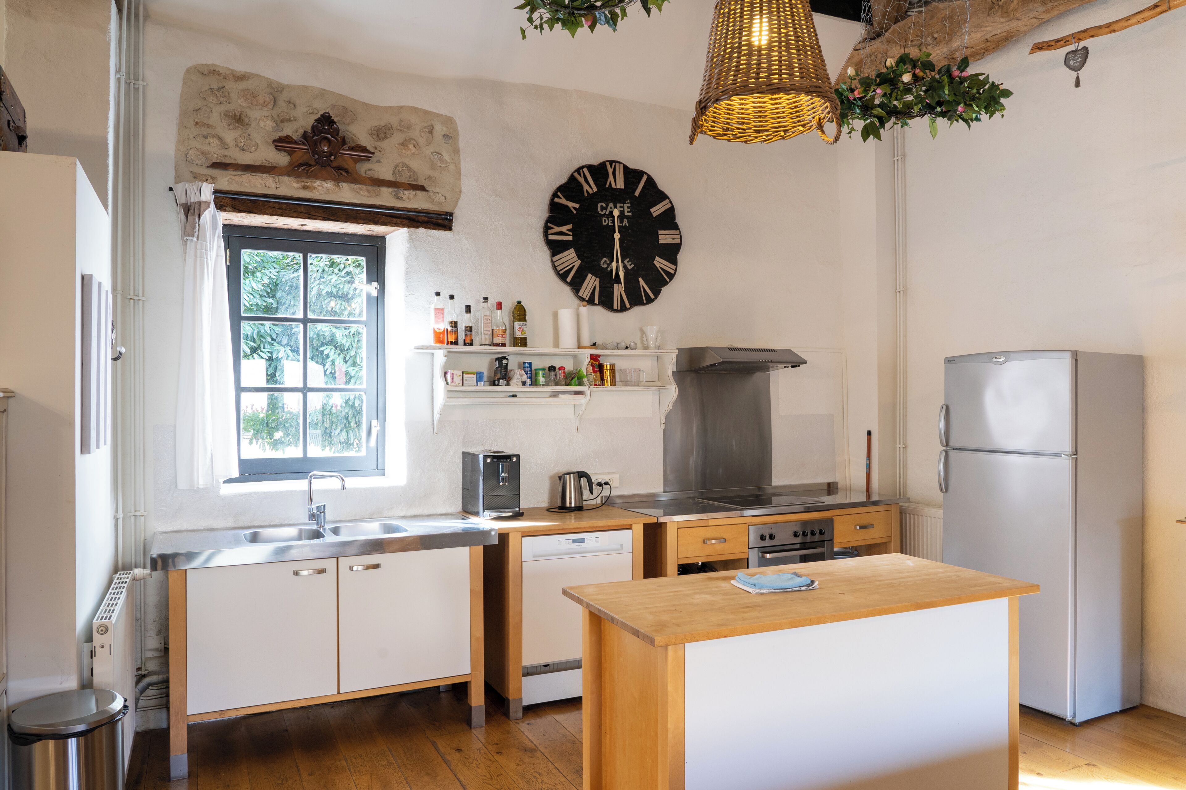 A kitchen with a wooden island, stainless steel appliances, a clock, and a window with a view of greenery.