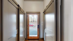 A hallway with a wooden door leading to an outdoor area with a car visible. - Amazing Riverfront Cabin with Views, Deck, Firepit, & Grill - Dog-Friendly (Vida)
