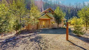 A lodge with a wooden exterior, a gravel driveway, and a mountain backdrop. - Amazing Riverfront Cabin with Views, Deck, Firepit, & Grill - Dog-Friendly (Vida)