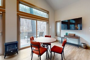 A room with a round table, four chairs, a fireplace, a TV, and large windows. - Amazing riverfront cabin with views, deck, firepit, & grill - dog-friendly (Vida)