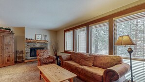 Un salon comprenant un canapé, une table basse en bois, une cheminée et une fenêtre avec des stores.