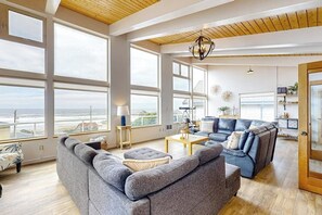 Un ampio soggiorno con ampie finestre, un lampadario moderno e vista sull'oceano.
