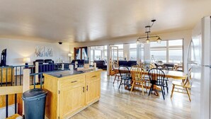 Una cocina amplia con una isla de madera, comedor con sillas y ventanas grandes.
