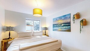 Un dormitorio con cama, dos lámparas de noche, una ventana y un cuadro de una vista marina.