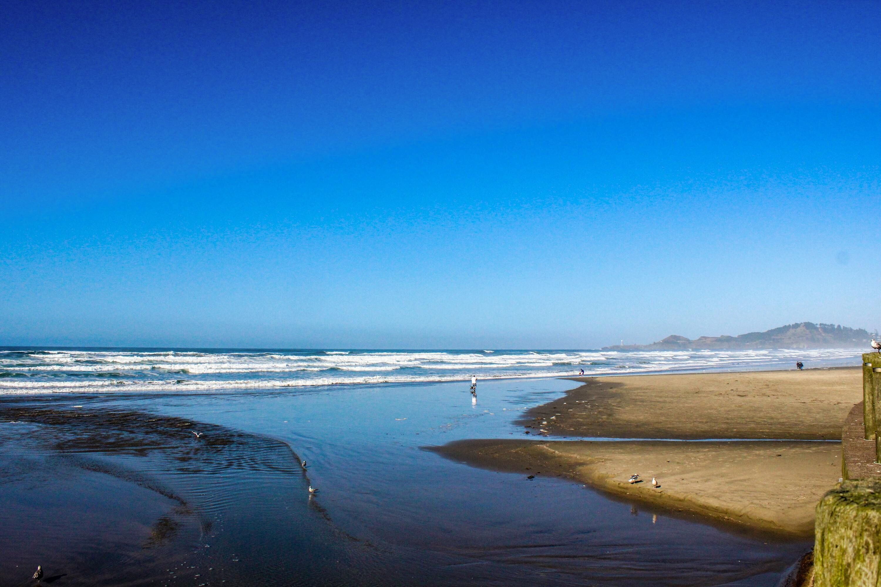 A beach with waves, a sandy shore, and a distant hill.