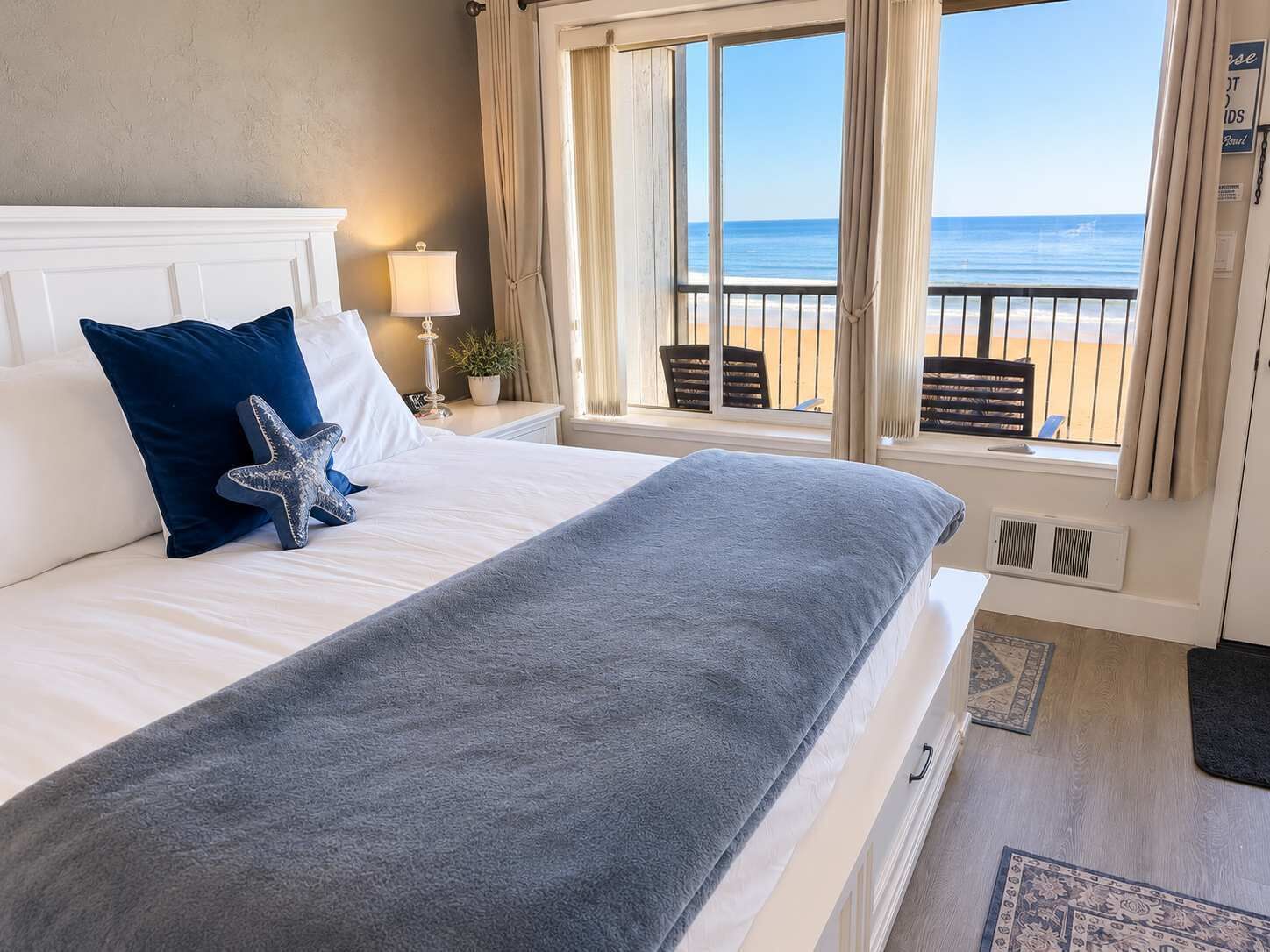 A hotel room with a large bed, a starfish decoration, a lamp, and a view of the beach.