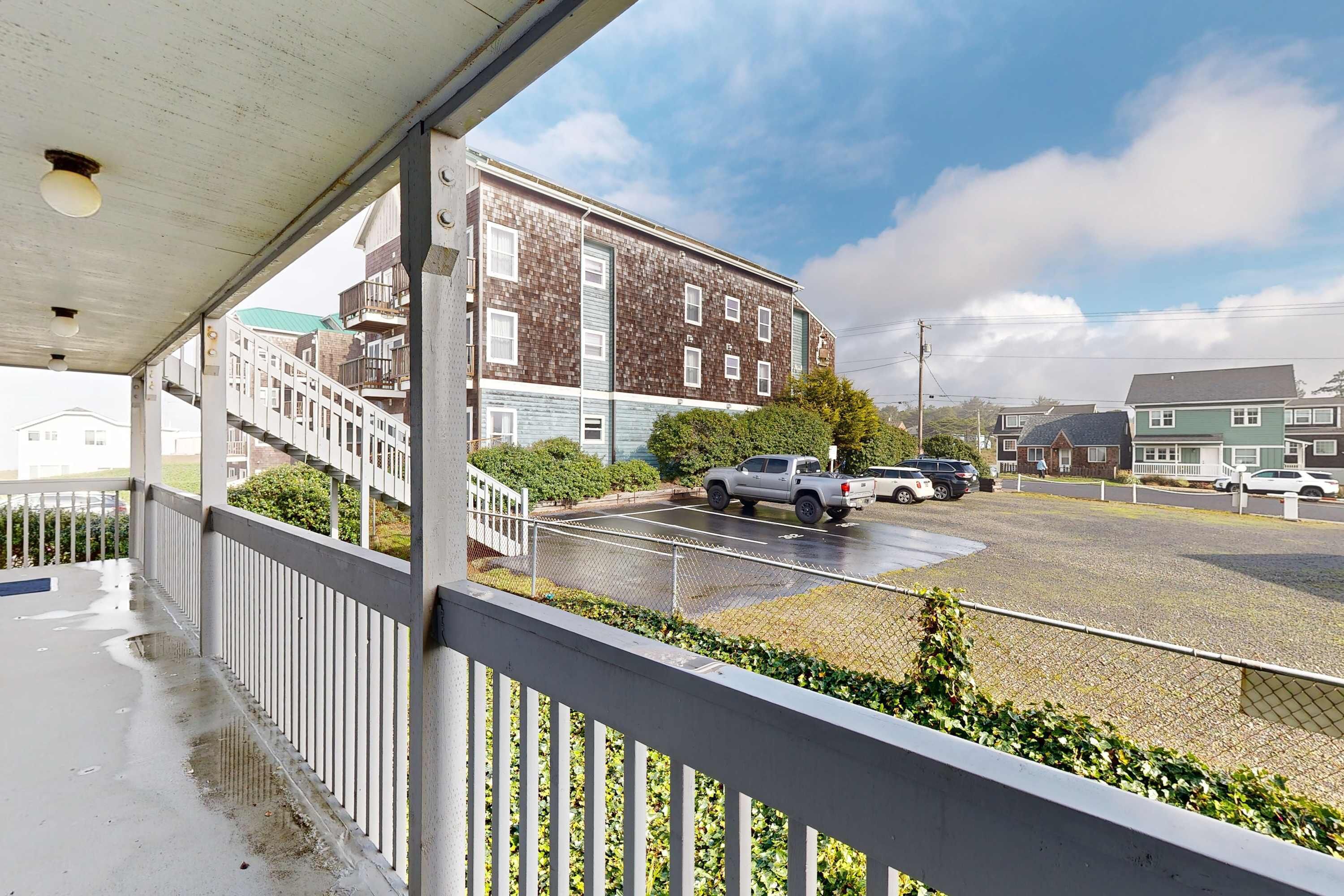 A covered balcony with a view of a parking lot and a building with multiple floors and balconies.