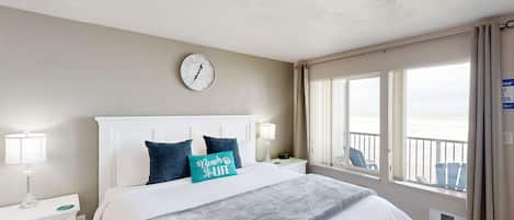 A hotel room with a bed, a clock, a window with a view, and a nightstand with a lamp.