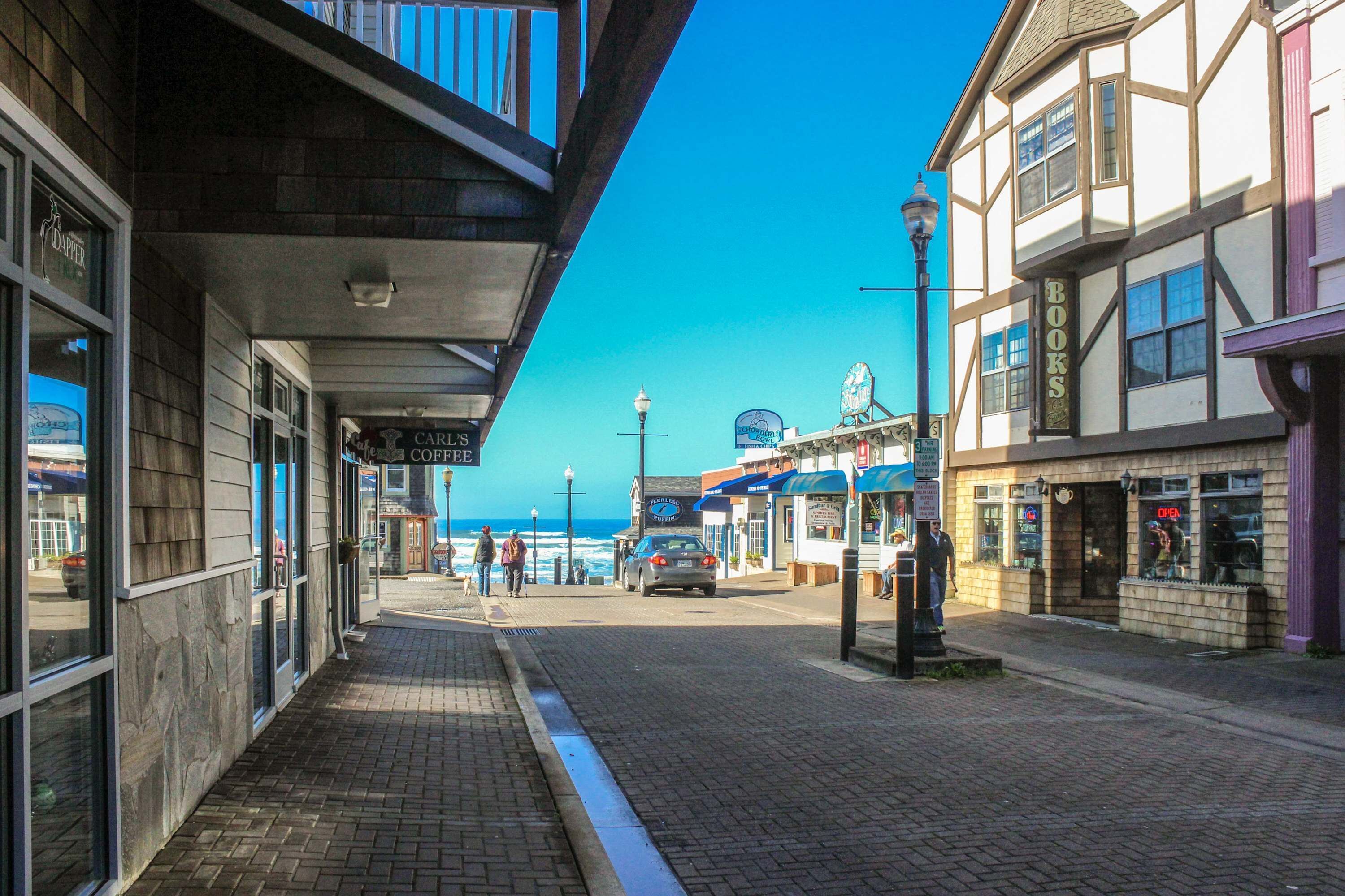 Une rue côtière bordée de boutiques, avec un café et une vue sur l’océan.