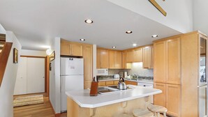 A modern kitchen with wooden cabinets, a central island with stools, a refrigerator, and a microwave. - Golf Course Views, Half Mile to the Village - Includes SHARC Access (Sunriver)