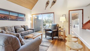 A living room with a sofa, armchair, coffee table, and a lamp. There is a sliding glass door leading to an outdoor area. - Golf Course Views, Half Mile to the Village - Includes SHARC Access (Sunriver)