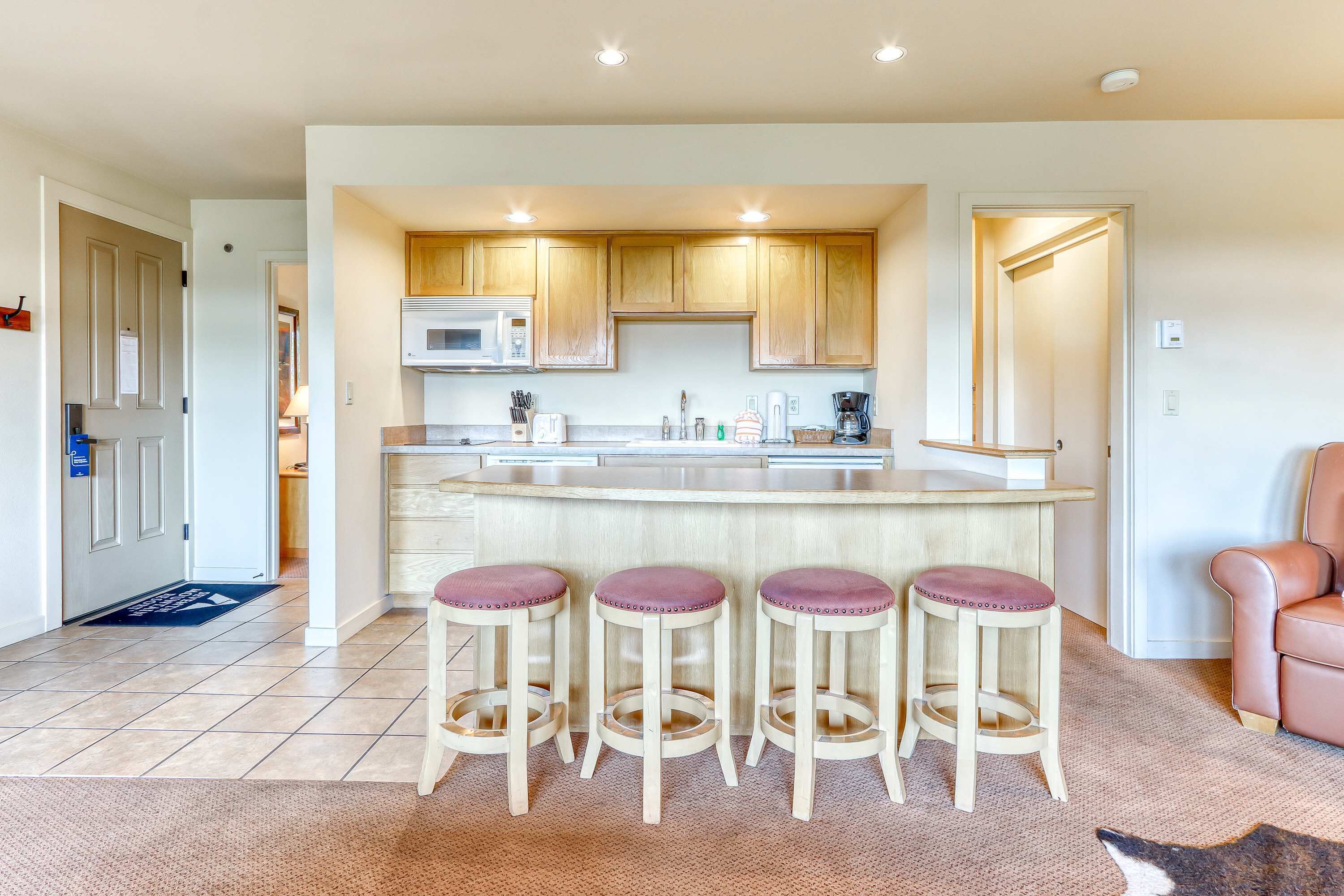 A kitchen with wooden cabinets, a central island with stools, and a microwave.