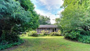 A house with a front yard, surrounded by trees and shrubs. - Dog-Friendly Cottage with Private Hot Tub, Deck, Berry Bushes, & Beach Access (Cannon Beach)
